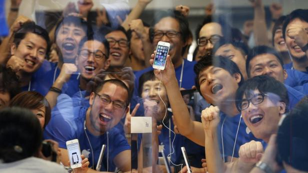 Eine Menschenmenge jubelt in einem Apple Store und hält iPhones in die Höhe.
