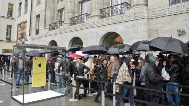 Menschen stehen mit Regenschirmen vor einem Geschäft Schlange, um das iPhone 5c zu kaufen.