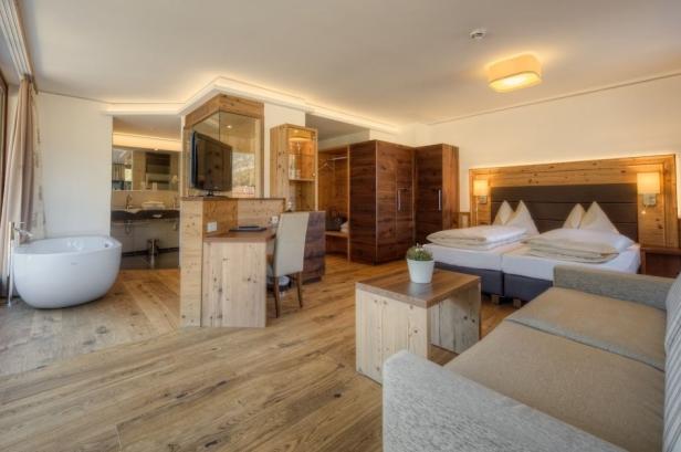 Ein modernes Hotelzimmer mit Holzboden, Badewanne und Doppelbett.