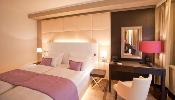 Ein helles Hotelzimmer mit Doppelbett, Schreibtisch und Sessel.