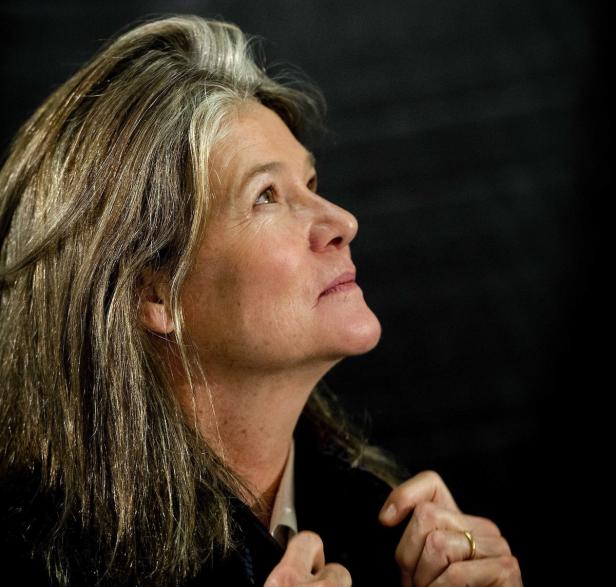 Eine Frau mit langen, graumelierten Haaren blickt nach oben.