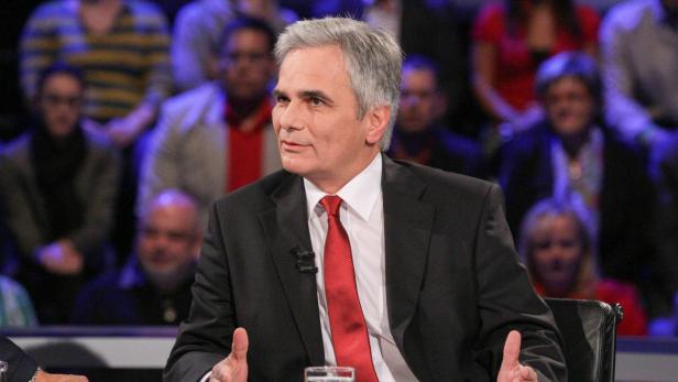 Ein Mann mit grauem Haar und roter Krawatte sitzt vor einem Publikum.