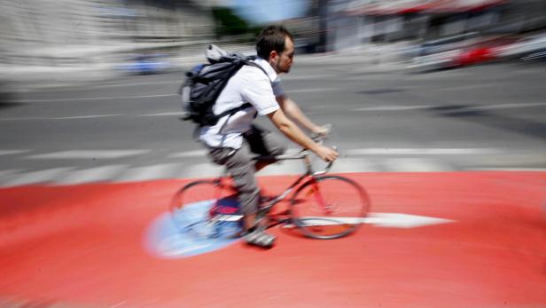 Ein Mann mit Rucksack fährt mit dem Fahrrad auf einem roten Radweg.