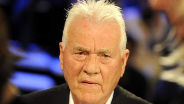 Nahaufnahme eines Mannes mit weißem Haar und ernstem Gesichtsausdruck.