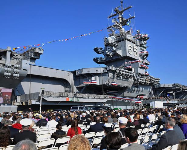 Eine große Menschenmenge sitzt vor dem Flugzeugträger USS Enterprise (CVN-65) bei einer Zeremonie.