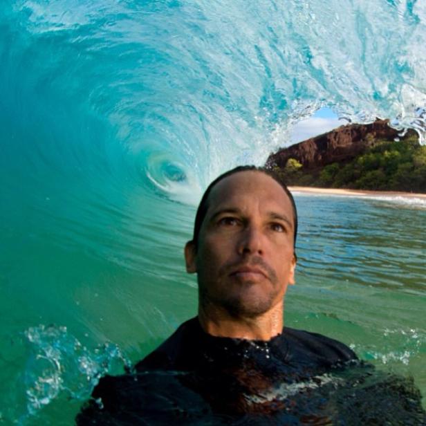 Ein Mann schwimmt im Meer, während eine Welle hinter ihm bricht.