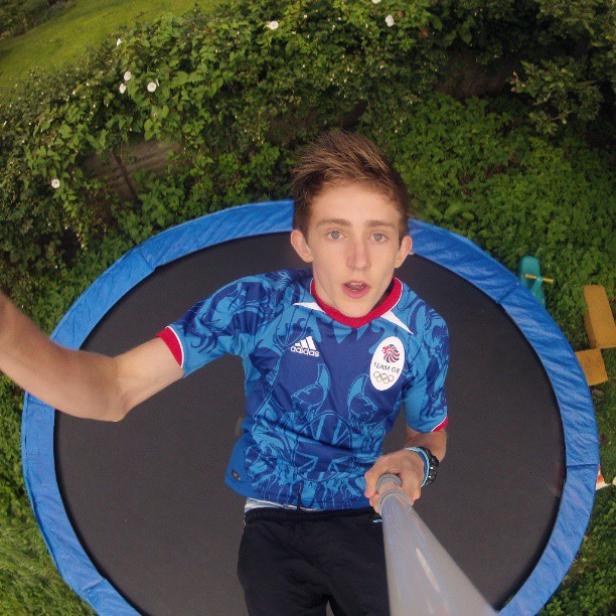 Ein junger Mann macht ein Selfie auf einem Trampolin im Garten.
