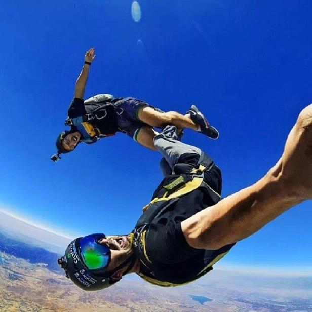 Zwei Fallschirmspringer im freien Fall vor blauem Himmel.