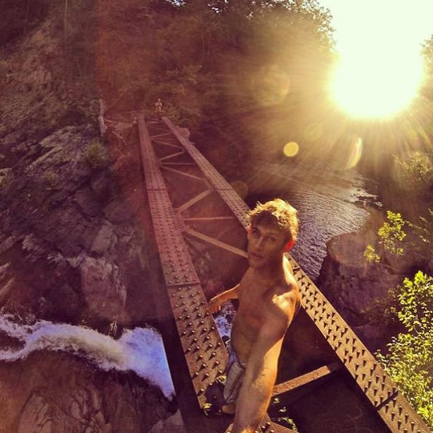 Ein junger Mann steht auf einer alten Eisenbahnbrücke über einem Fluss.