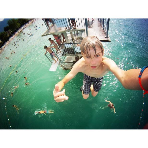 Ein Junge springt von einem Sprungturm in einen See.