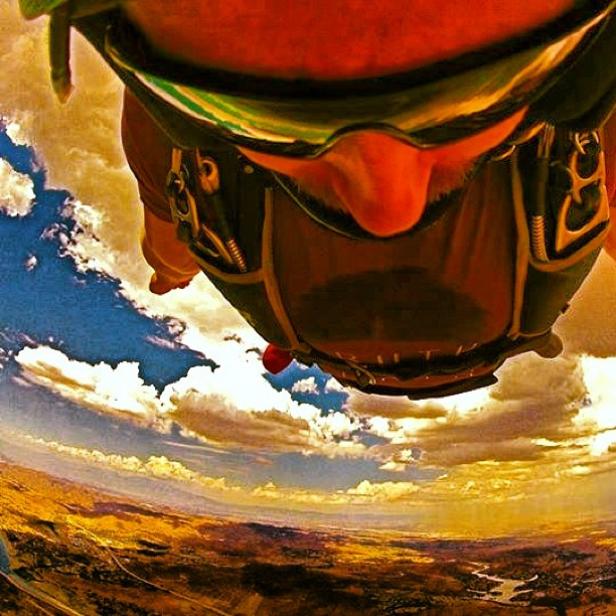 Ein Fallschirmspringer im Himmel über einer Landschaft.