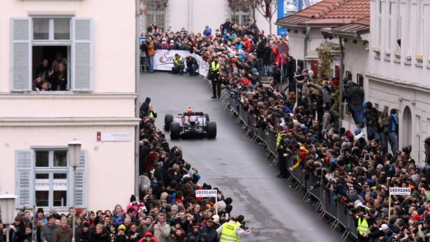 Ein Formel-1-Wagen fährt durch eine Menschenmenge in der Stadt.