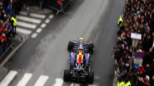 Ein Formel-1-Rennwagen fährt durch eine Menschenmenge auf einer städtischen Straße.