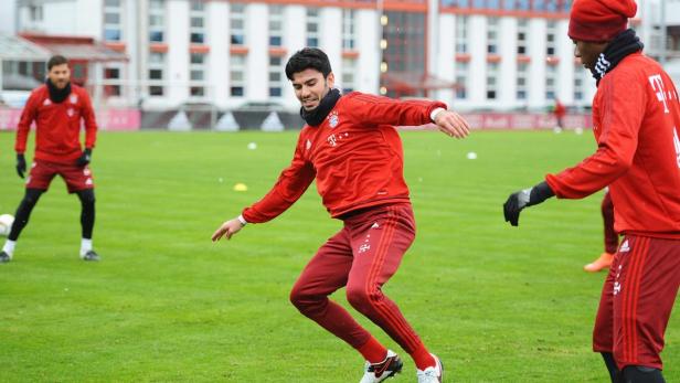 Ein Fußballspieler in roter Trainingskleidung dribbelt auf einem grünen Rasen.