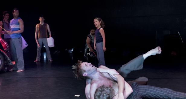 Eine Theaterszene mit mehreren Darstellern auf einer dunklen Bühne.