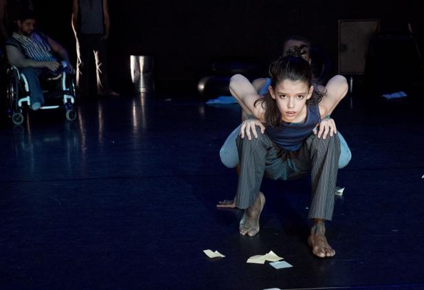 Eine junge Tänzerin in ungewöhnlicher Pose auf einer dunklen Bühne.
