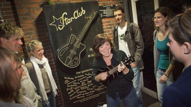 Eine Frau spielt Ukulele vor dem Star-Club-Denkmal in Hamburg mit Gästen wie den Beatles.
