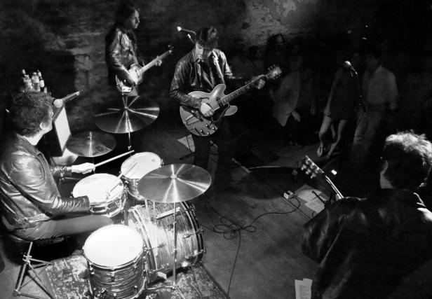 Eine Band spielt in einer dunklen Bar vor Publikum.