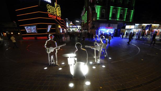 Eine belebte Straße in St. Pauli mit einer Skulptur einer Band im Vordergrund.