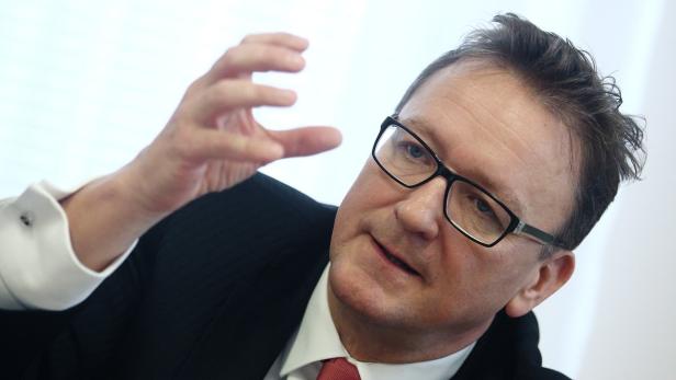 Ein Mann mit Brille und Anzug gestikuliert mit der Hand.