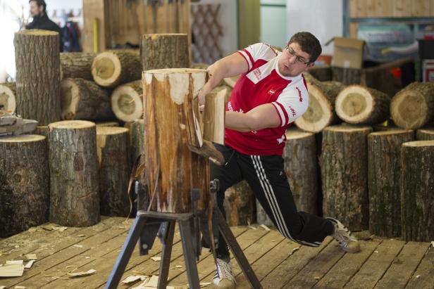Ein Mann spaltet einen Baumstamm mit einem Keil und einem Hammer.