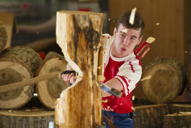 Ein junger Mann spaltet mit Axt und Keil einen Baumstamm.