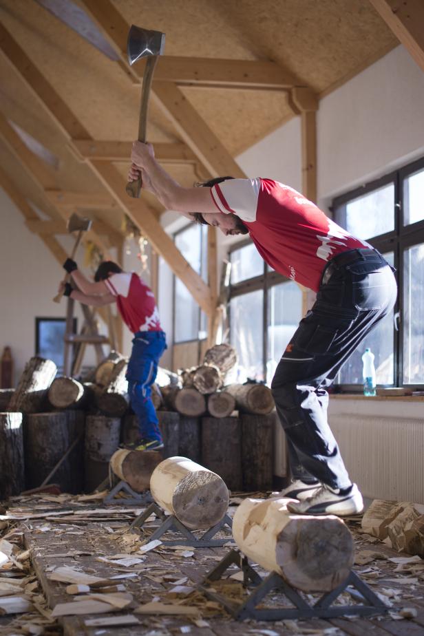 Zwei Männer spalten Holz mit Äxten in einem hellen Raum.