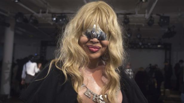 Eine Frau mit blonder Perücke und silberner Maske posiert für ein Foto.