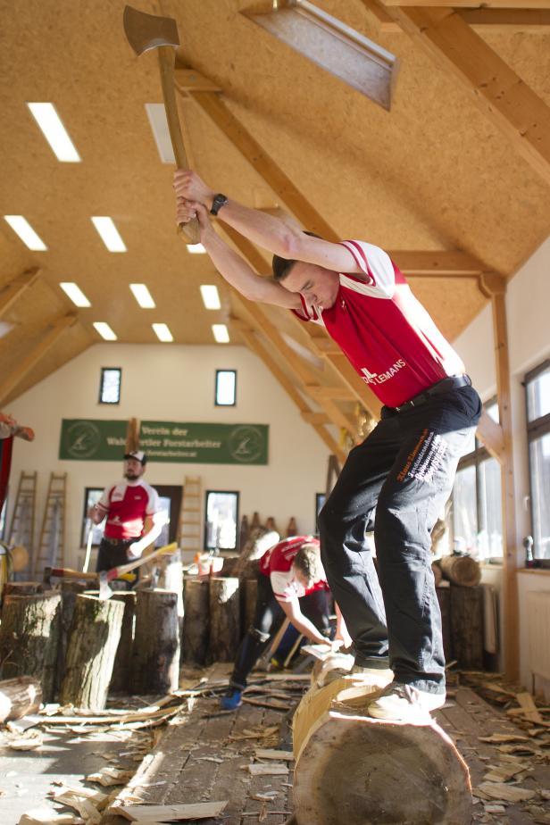 Ein Mann steht auf einem Baumstamm und schwingt eine Axt über dem Kopf.