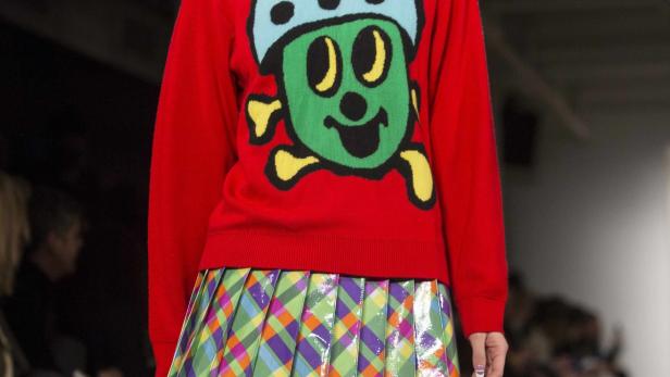 Ein roter Pullover mit einer grünen Comicfigur und ein bunter Faltenrock.