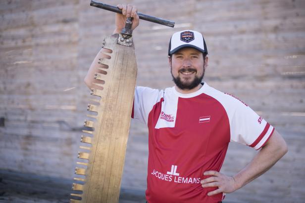 Ein Mann mit Bart hält eine große Holzsäge in die Höhe.