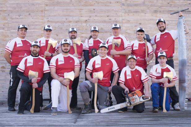 Eine Gruppe von Holzfällern posiert mit Äxten und einer Kettensäge für ein Foto.