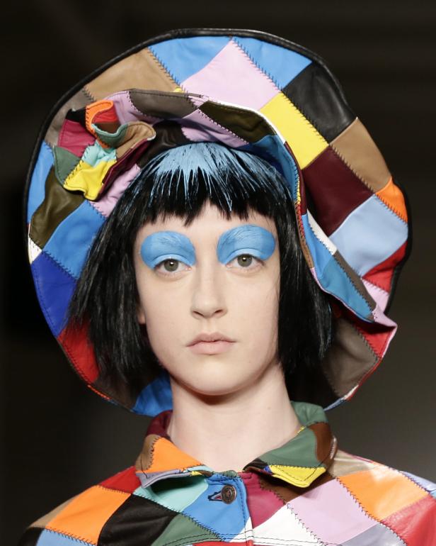 Ein Model mit blauem Lidschatten und einem bunten Patchwork-Hut.