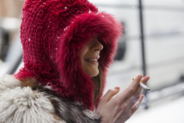 Eine Frau mit roter Pelzmütze raucht eine Zigarette.