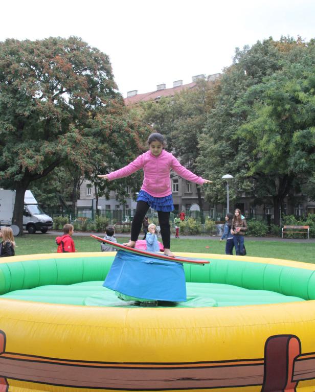 Ein Mädchen balanciert barfuß auf einem Surfbrett in einem aufblasbaren Becken.