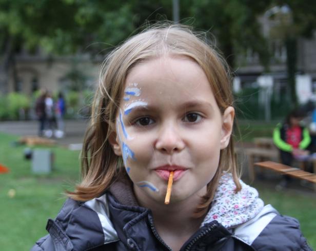 Ein Mädchen mit Gesichtsbemalung hält einen Keks im Mund.