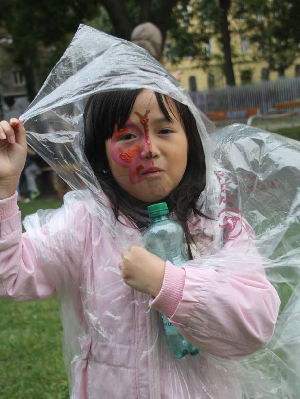 Ein Mädchen mit Gesichtsbemalung trägt eine Plastikplane über dem Kopf und hält eine Wasserflasche.
