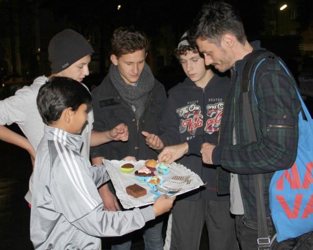 Ein Junge bietet einer Gruppe von Jugendlichen und einem Mann Muffins auf einem Tablett an.