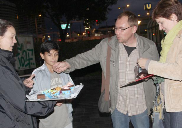 Ein Junge bietet Passanten auf der Straße Cupcakes an.