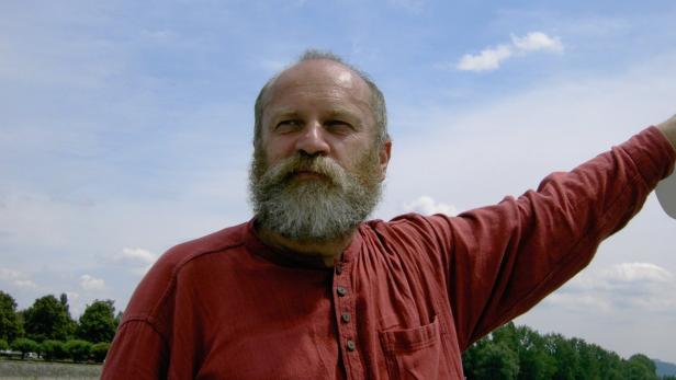 Ein Mann mit Bart und rotem Hemd vor einem bewölkten Himmel.