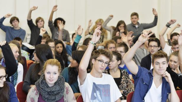 Viele Studenten sitzen in einem Hörsaal und heben die Hände.