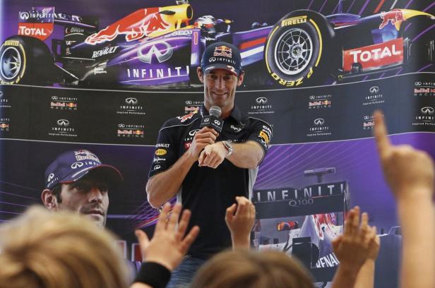Mark Webber spricht vor einem Hintergrund mit einem Red Bull Formel-1-Rennwagen.