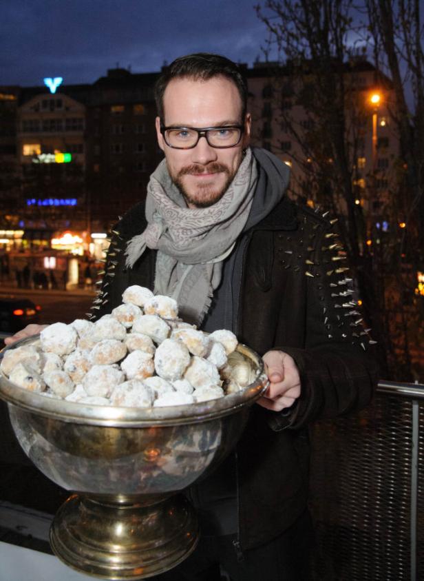 Ein Mann mit Brille hält eine große Schale voller Puderzucker-Kekse.