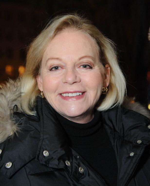 Eine lächelnde Frau mit blonden Haaren und einer schwarzen Jacke.