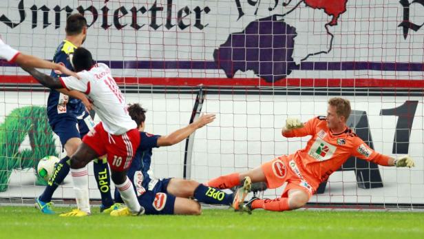 Ein Fußballspiel mit einem Torwart in orangefarbener Kleidung, der einen Schuss abwehrt.