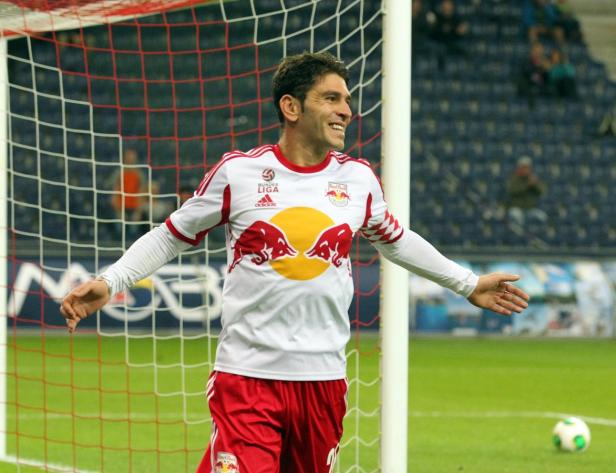 Ein lächelnder Fußballspieler im Trikot von Red Bull Salzburg steht vor einem Tor.
