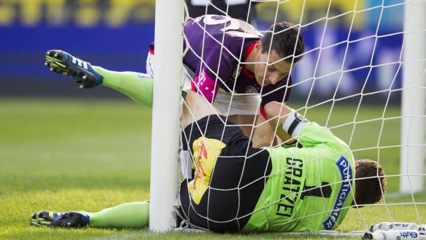 Ein Fußballspieler und ein Torwart ringen im Tor miteinander.