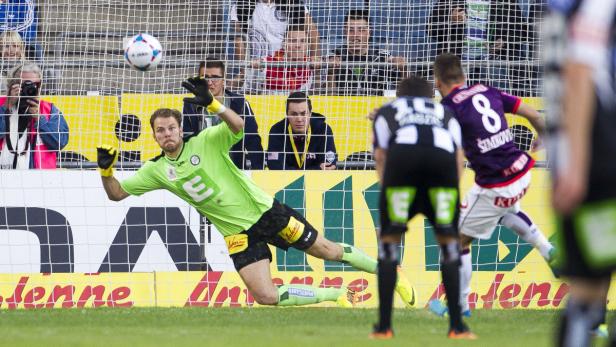 Ein Fußballtorwart in Grün wehrt einen Ball ab.
