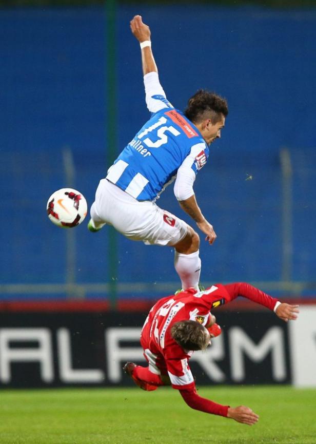 Ein Fußballspieler springt über einen am Boden liegenden Gegenspieler, um den Ball zu erreichen.