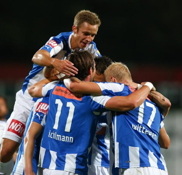 Eine Gruppe von Fußballspielern in blau-weißen Trikots umarmt sich jubelnd.